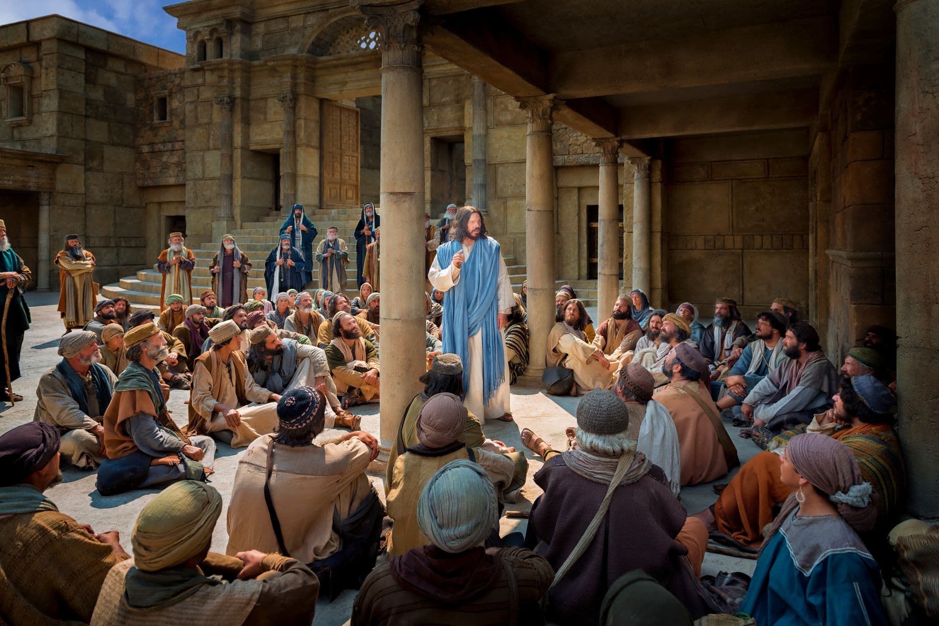 Jesus Christ in a blue robe teaching a large crowd seated on the ground in a stone courtyard.